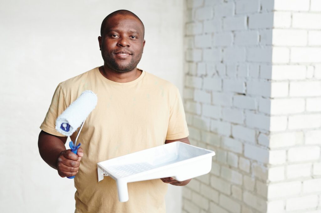 African Man Painting Wall Demonstrating Flat Vs Satin Paint Resized