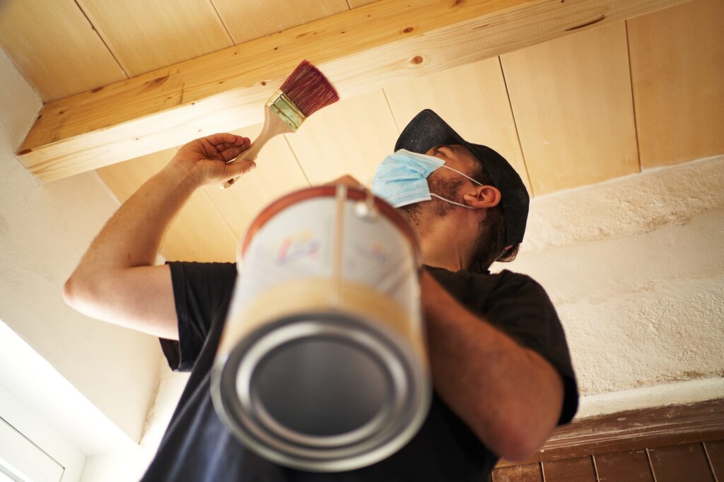 Hispanic Man Applying Satin Paint On Wooden Beam At Home Resized